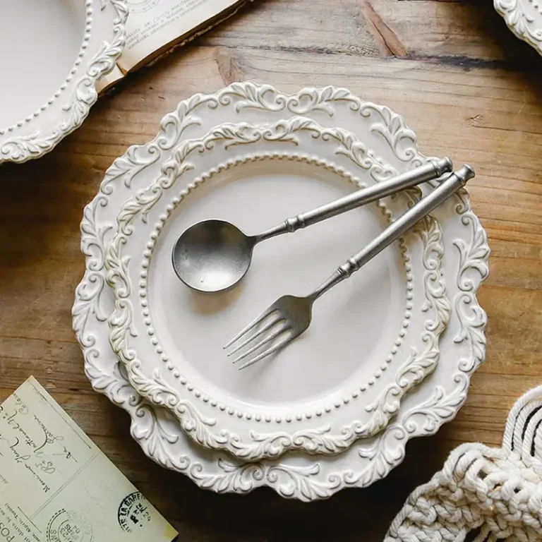 Two vintage silver utensils placed on top of two stacked antique cream colored plates on a wooden surface.