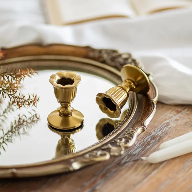 Two brass candlestick holders on an ornate mirrored tray.