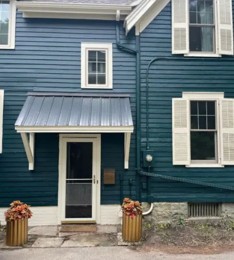 A side view of a Victorian home painted a bluish green color with white shutters.