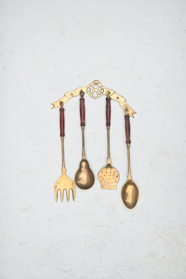 Vintage copper utensils hanging on an antique wall hanger on a textured white wall.