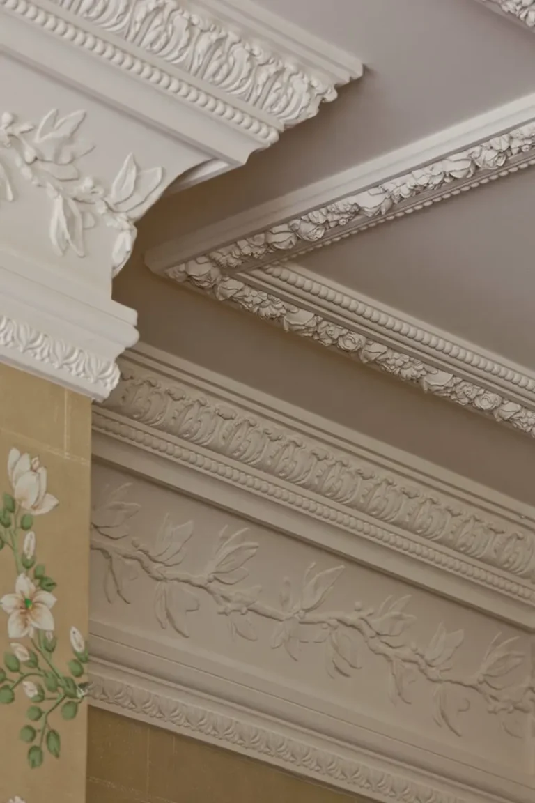 Decorative white crown and ceiling molding paired with a partially seen mustard yellow wall with floral designs.