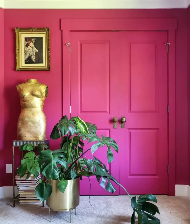 A lively pink vintage-style door and wall with a gold dress form and a big monstera plant in front of it.