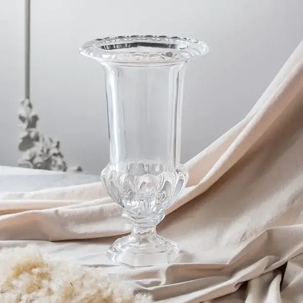 An antique-style glass flower vase on a piece of grayish-pink curtain.