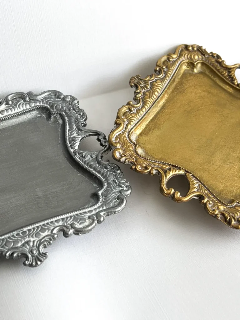 Two silver and gold ornate jewelry trays on a white surface.