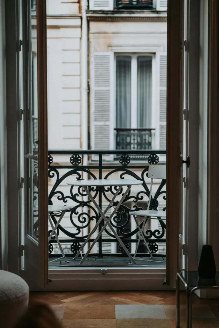 French double doors open onto a balcony with a table and two chairs.