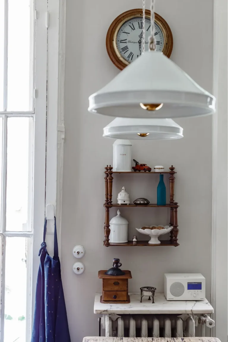 White pendant lights, a vintage wooden shelf with vintage-style kitchen accessories, an old-fashioned coffee grinder, and a dark blue apron.