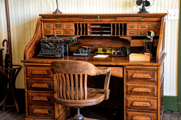 An old-fashioned wooden vintage office desk with various vintage items on it and an old wooden swivel chair in front of it.