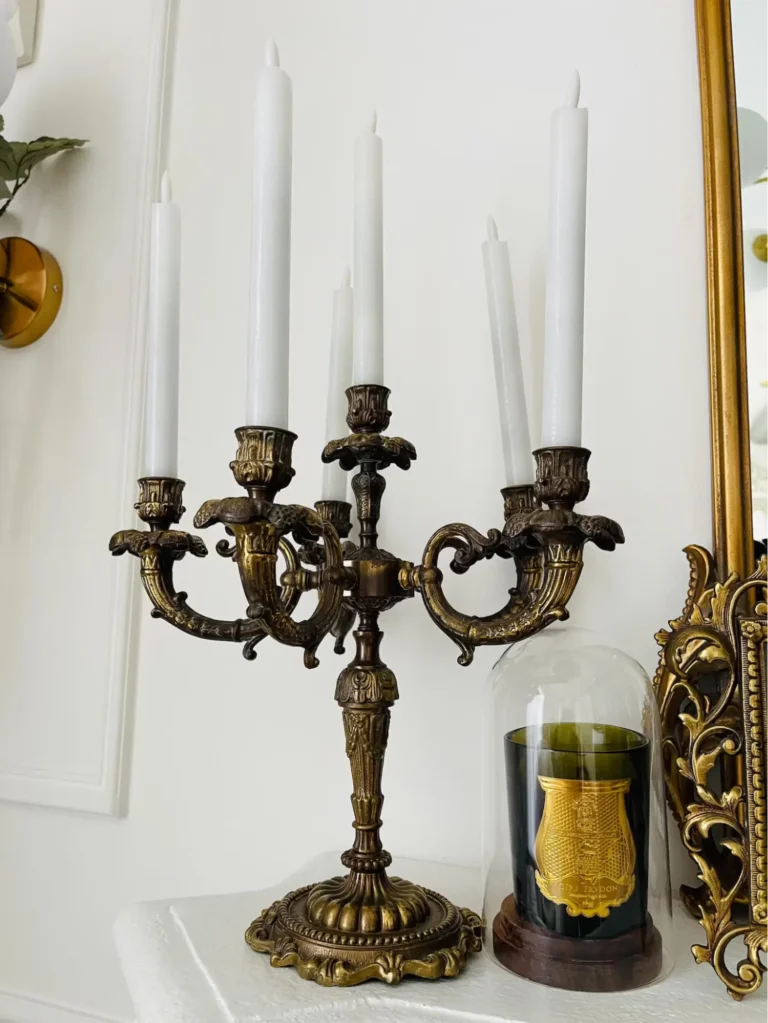 An antique bronze candelabra with white candles; a small glass cloche with a green-glass candle underneath stands next to the candelabra.