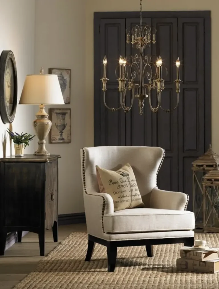 A vintage French decor interior with a cream-colored armchair with a French-labeled throw pillow, a jute rug, an antique-style chandelier, an antique console, lanterns, a round vintage wall clock, and a stack of books.