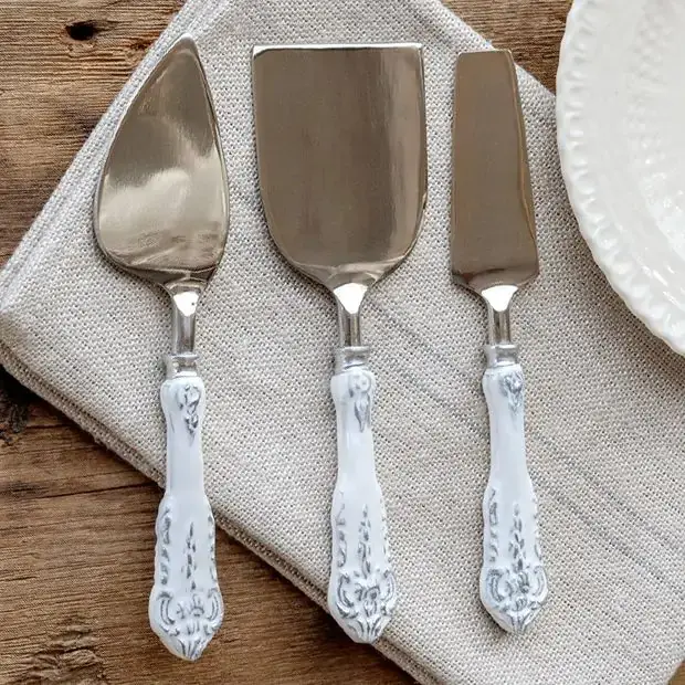 Three antique-style cheese servers lined up next to one another on a beige linen fabric.