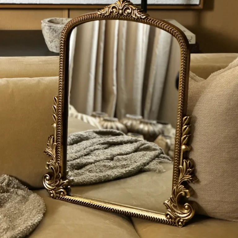 A rectangular ornate brass mirror with a rounded top sitting on a beige-colored couch.