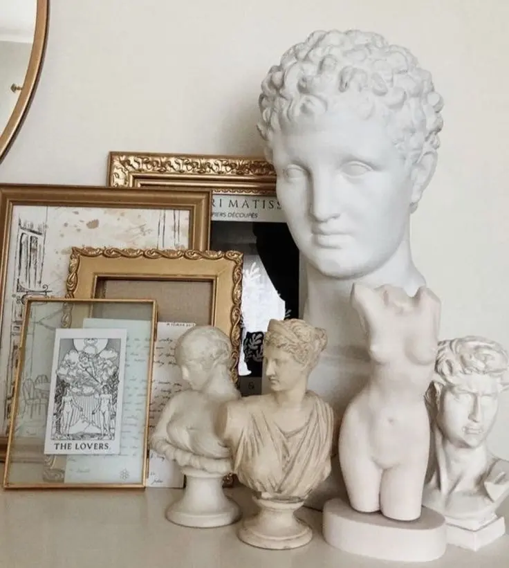 A collection of ivory-colored bust sculptures in front of a display of ornate gilded frames.