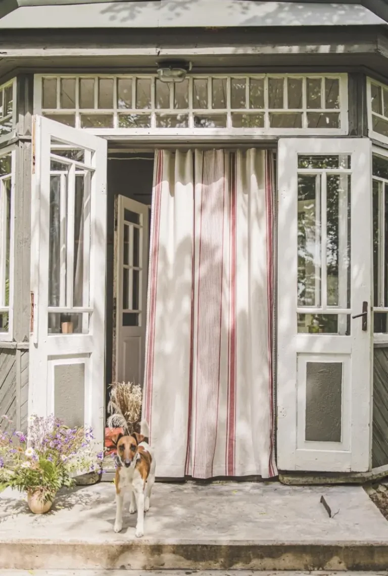 A vintage porch with double wooden white doors and a French striped red linen curtain.