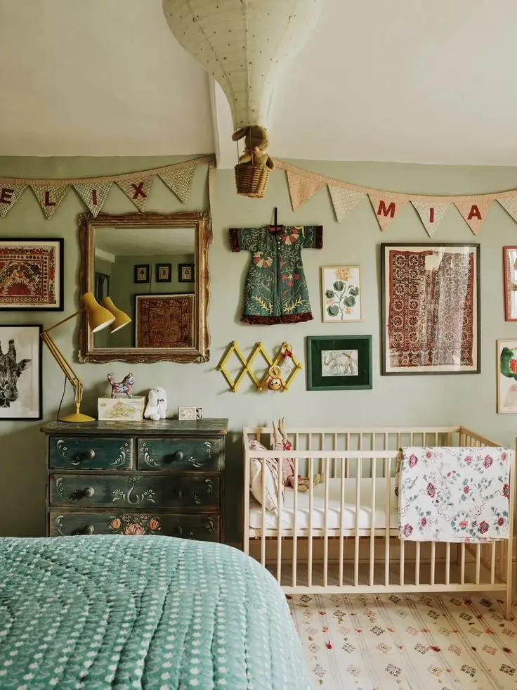 A green vintage nursery with a wooden crib, a dark green antique dresser, a vintage-inspired bunting, gallery wall, mirror, and a hot air balloon decoration.