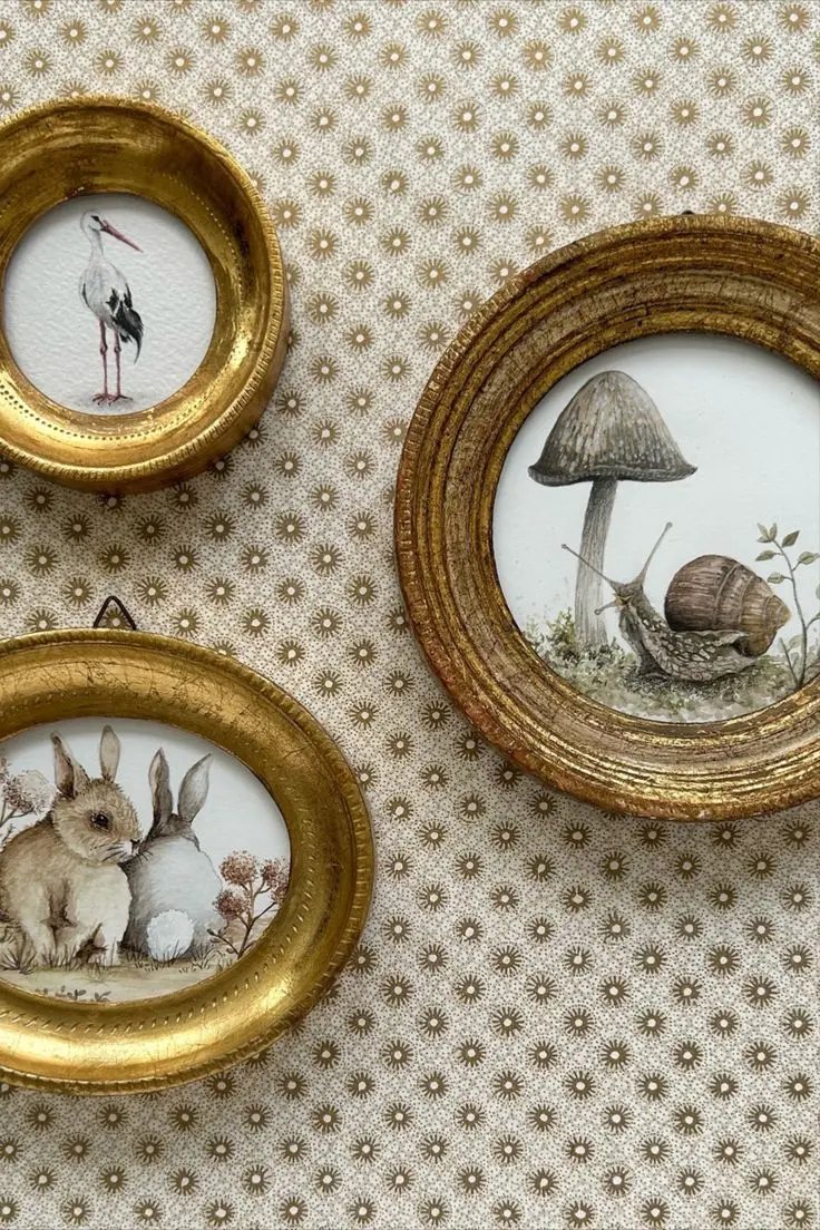 Vintage nursery animal illustrations in round and oval gilded frames hang on a patterned wallpaper.