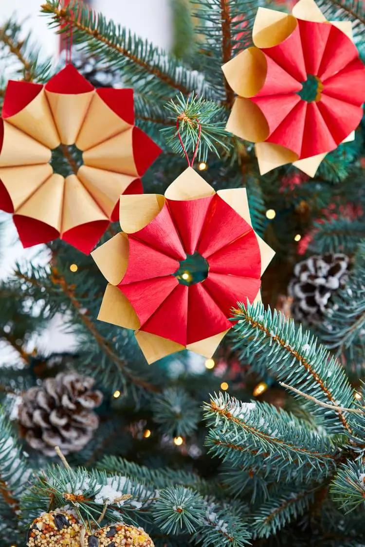 Three vintage paper ornaments hanging on a Christmas tree with two pinecones visible in the background.