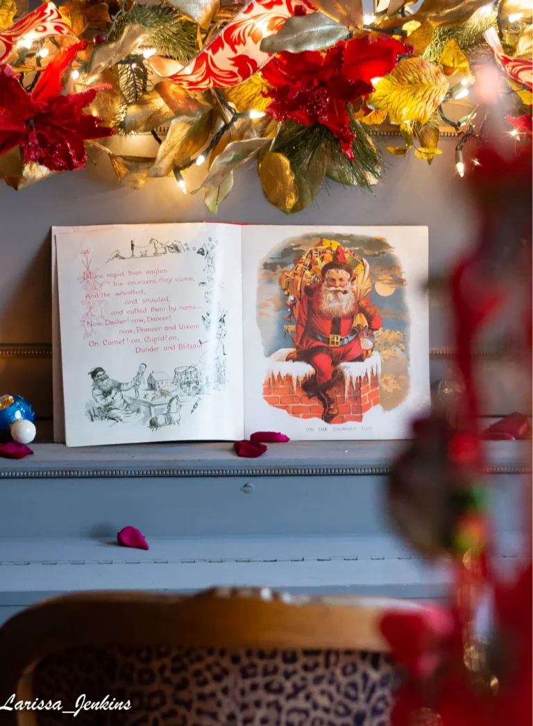 A vintage book featuring Santa Claus is sitting open on top of an old gray-colored piano, with a poinsettia and string lights garland on top.