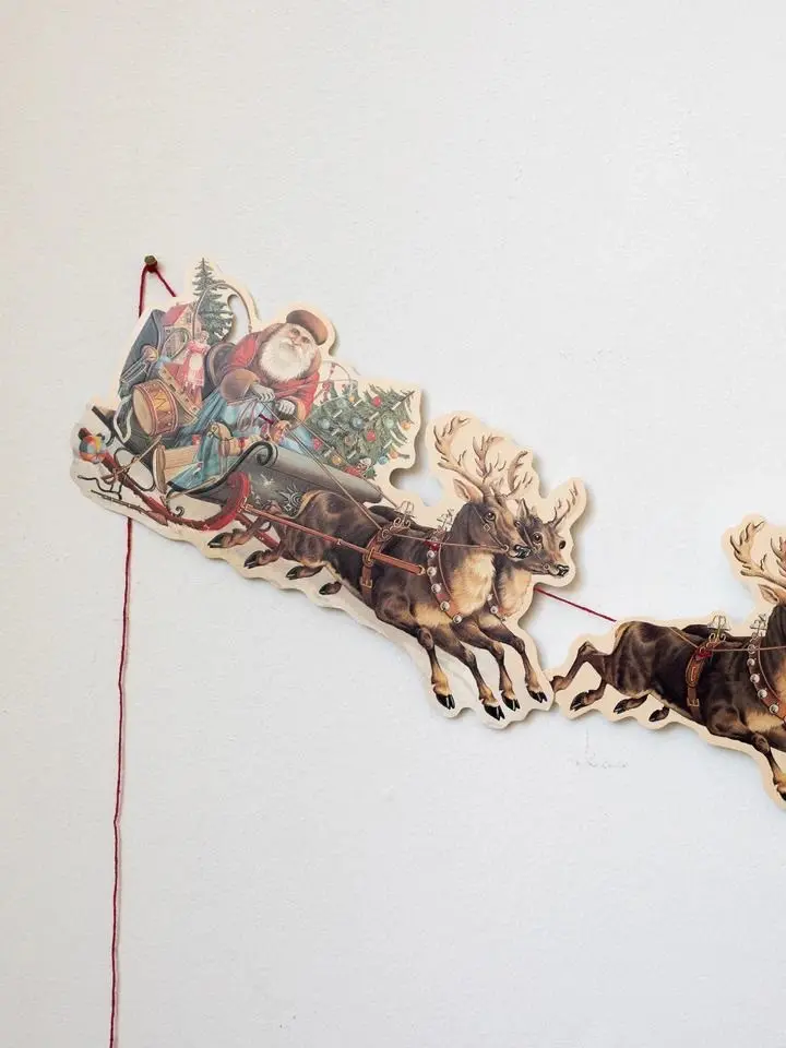 A closeup view of a vintage paper Christmas bunting featuring Santa Claus surrounded by Christmas presents on a sleigh with reindeer.