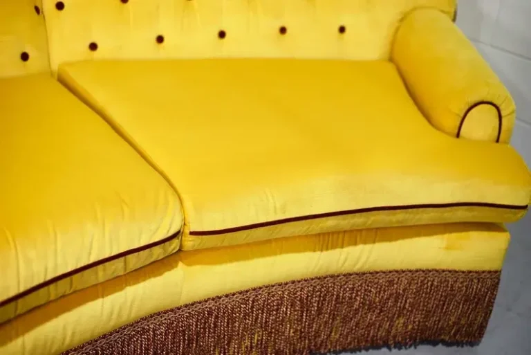 A closeup photo of a yellow vintage Hollywood glam sofa with fringes.