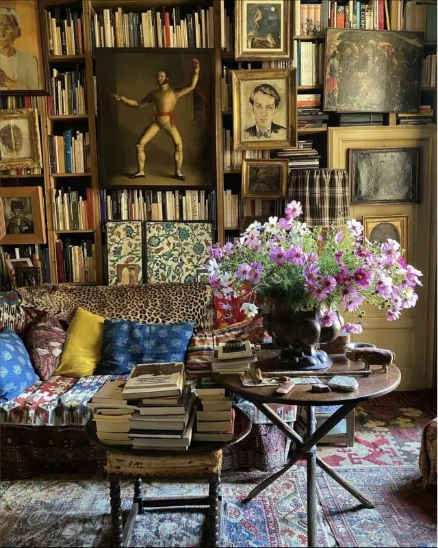 Vintage Italian maximalist decor in Milan apartment featuring layered paintings, antique bookshelves, richly patterned upholstery, and textured accents.