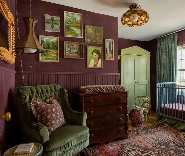 Vintage maximalist decor nursery with a green armchair, antique dresser, eclectic wall art, and warm jewel tones.