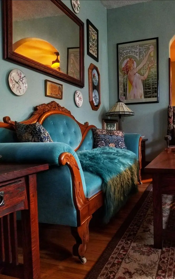 Vintage maximalist decor with an ornate blue velvet sofa, eclectic wall art, and antique wooden furniture in a cozy living room.