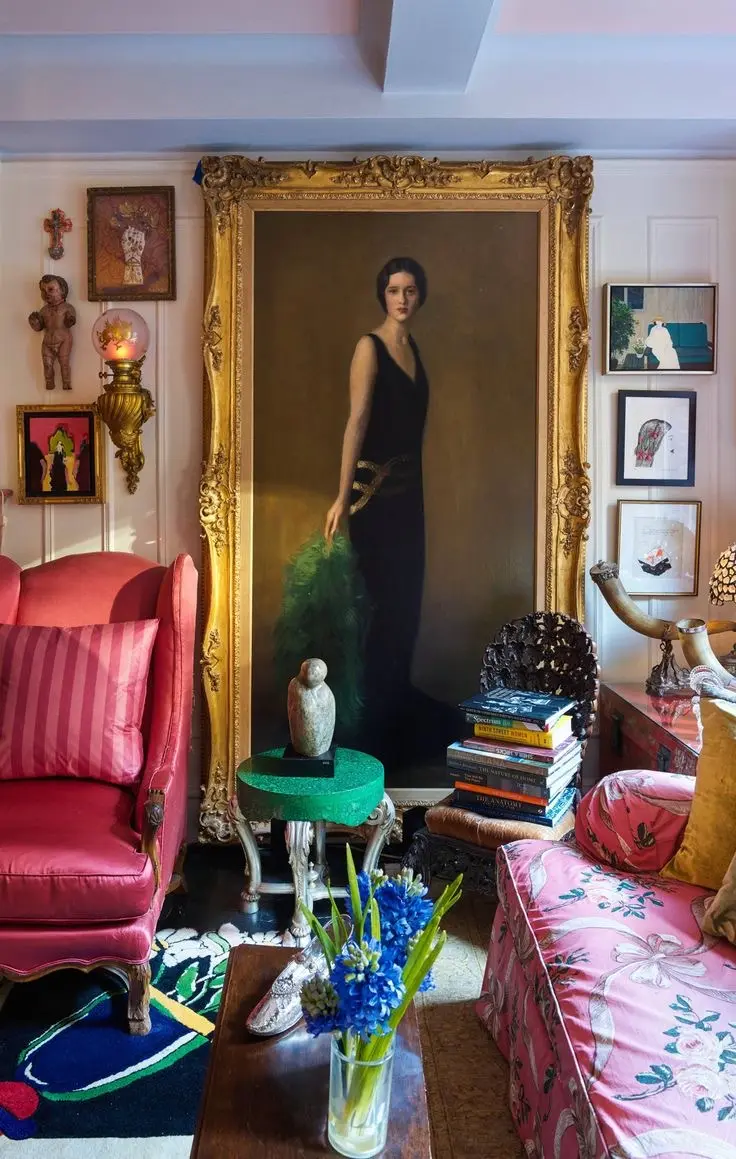 Vintage maximalist decor living room with an oversized portrait, pink velvet armchair, floral sofa, and an eclectic wall art gallery.