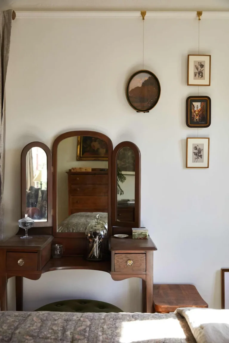 Eclectic vintage bedroom with a 1920s vanity dresser, layered artwork, and collected decor accents.
