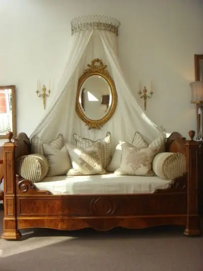 Cozy vintage bedroom daybed with carved wood frame, lace canopy, and antique mirror.